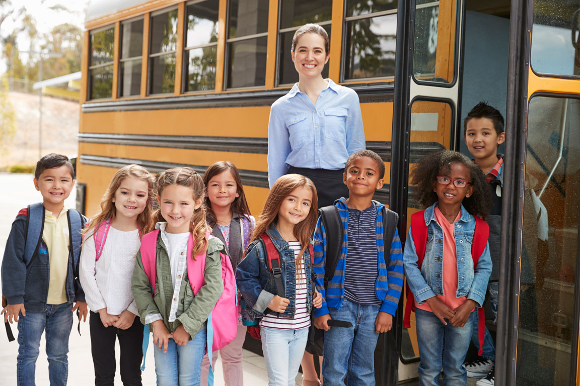 elementary school teacher standing next to school bus with her students